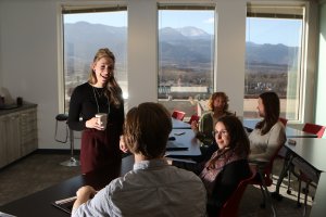 Woman in dialogue with colleages in office classroom overlooking CO mountains